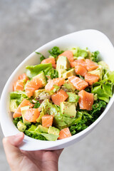 Salmon salad with green leaves and avocado on oval white bowl.