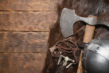 Viking axe, armor helmet and beast skin on the wooden table flat lay background with copy space.