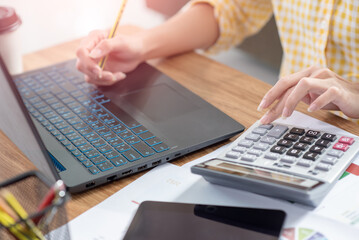 Close up of a businesswoman hands typing in a laptop and using calculator at her house, working at home, business concept