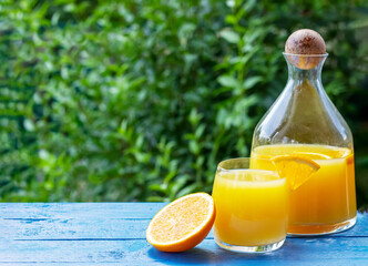 Fresh orange juice in pitcher and glass with ripe oranges on the blue wooden table