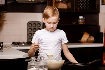 Teenage Boy in the kitchen at home making dough for pancakes pastry. Children cooking concept.