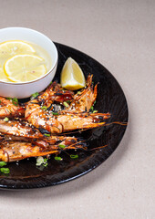 Close-up with a delicious snack. Grilled shrimp on beautiful black plate. Water and lemon.