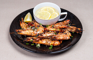 Close-up with a delicious snack. Grilled shrimp on beautiful black plate. Water and lemon.