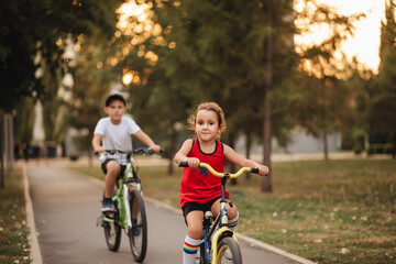 Fototapeta premium Two little boy and girl cyclists riding their bikes and enjoy having fun. Kid outdoors sport summer activity.