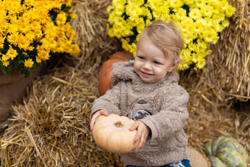 A small child holds a pumpkin in his hands on a background of hay