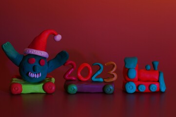 A toy train with the number 2023 and a coronavirus figurine. Festive event, Christmas and New Year. A symbol of the advent of holidays. Bright colored background.