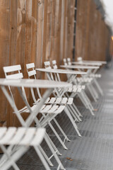 White chairs and tables after a rainy day on a brown wall background. - obrazy, fototapety, plakaty