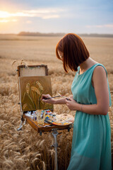 Woman artist painting with oil paints in wheat field during sunset. Getting inspiration from...