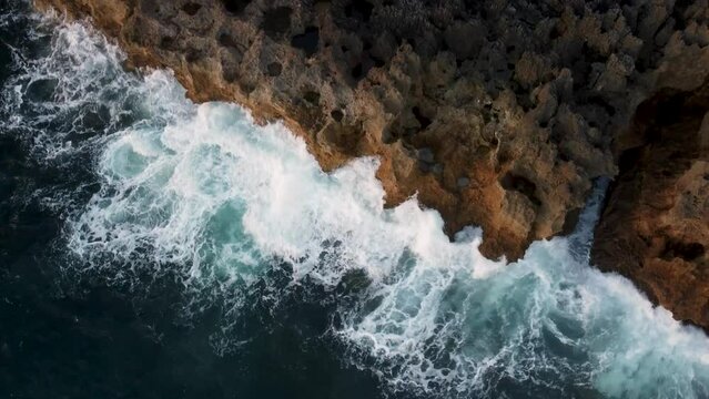 4k Drone view from above of giant ocean waves crashing and foaming on empty sand tropical beach with big rock stones.