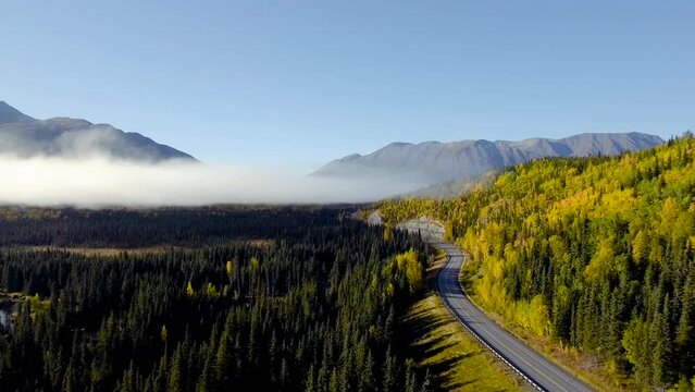 Sunny autumn morning near Cooper Landing, Alaska. Aerial view of forest Sterling Highway with mountains in distance.