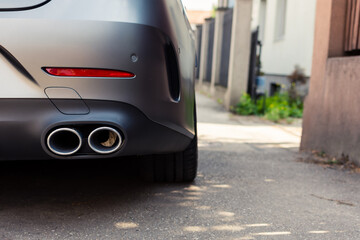 Double exhaust pipe of a modern gray parked car next to a building
