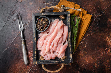 Uncooked Raw chicken meat slices in a wooden tray with herbs. Dark background. Top view