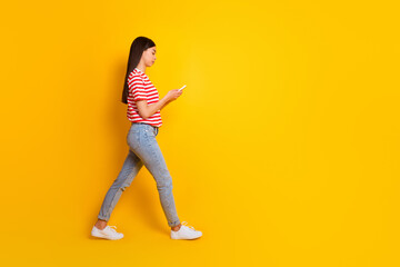 Fototapeta na wymiar Full size profile portrait of pretty person walk hold use telephone empty space isolated on yellow color background