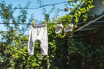 Baby clothes socks and pants for a newborn are hung on a rope with clothespins on a background of blue sky and leaves