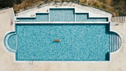 Girl relaxing in a pool with her face covered with a hat, top down view from a drone