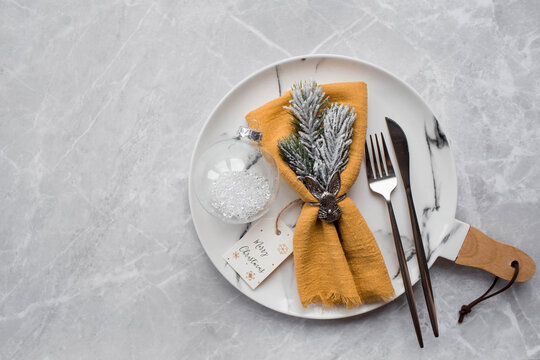 Table setting. A marble plate with a rabbit on a napkin, branches of a Christmas tree and Christmas decorations on a gray background. The concept of Merry Christmas, New year 2023 and restaurants.