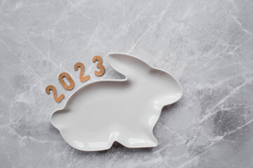 Fototapeta premium Table setting. A plate in the form of the symbol of the year 2023 rabbit, and cutlery on a gray marble background. The concept of Merry Christmas, New Year 2023 and restaurants.
