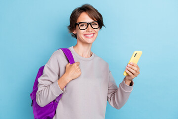 Photo of cheerful positive pretty lady hold bag telephone modern device gadget stand empty space isolated on blue color background