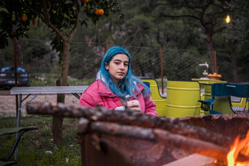 woman sitting at campsite smiling at camera, outdoor photos of marginal and young woman sitting in green natural environment