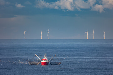 A cutter with lifted drag nets on the North sea with wind turbines in the background