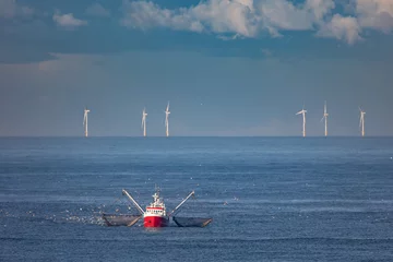 Foto auf Acrylglas A cutter with lifted drag nets on the North sea with wind turbines in the background © jokuephotography