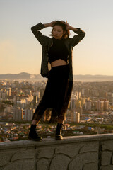 Fashionable Asian girl standing on concrete wall with sunset city background.