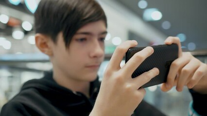 Caucasian boy using smartphone gadget social media mobile application on cell phone in shopping centre and playing games. Digitalization and informatization of society in modern urban world