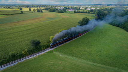 Drone View of an Antique Steam Engine, Approaching, Blowing Steam and Traveling Along the Countryside on a Sunny Day