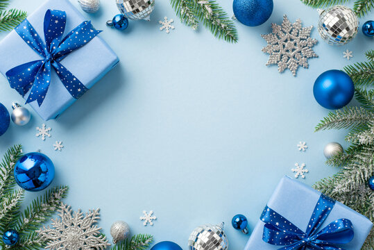 Christmas concept. Top view photo of blue silver baubles disco balls snowflake ornaments present boxes with bows pine branches confetti on isolated light blue background with empty space in the middle