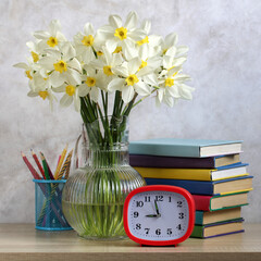 Goodbye, school! A composition with daffodils, textbooks and an alarm clock.
