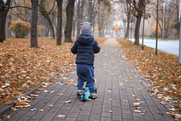 happy child 2 years old rides a scooter in autumn. Outdoor games during the cold season.