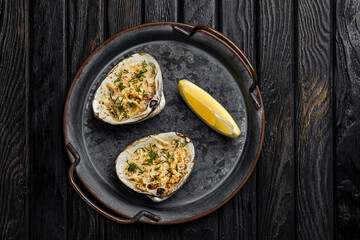 Oysters baked with cheese and herbs served with lemon on a rustic metallic plate