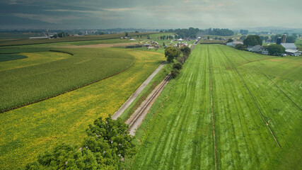 Drone View of Amish Countryside With Barns and Silos and a Single Railroad Track Traveling Through It, on Sunny Day.