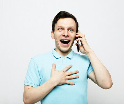 Happy Young Man Holding A Phone To His Ear, Listening To The News. The Man Rejoices, Pressing His Hand To His Chest.