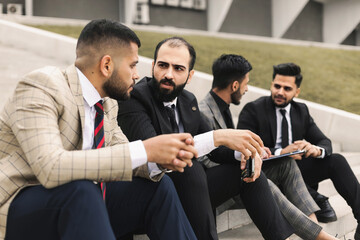Business people outdoor meeting. Several men in suits sit on the steps of a street staircase during a work break. Successful promotion and recognition in the team of employees.