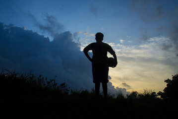 Silhouette of boy playing football during sky sunset background, Silhouette Boy Standing On Field Against blue cloudy Sky
