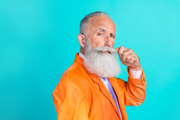 Photo of attractive charismatic man dressed trendy orange outfit hand touch mustache stand empty space isolated on cyan color background