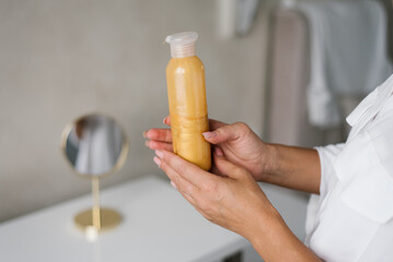 Close-up of a gold-colored moisturizer in the hands of a woman woman
