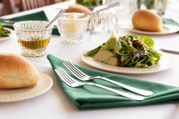 Fine dining table setting; plated salad, dinner rolls and various dressings with various plates and silverware.