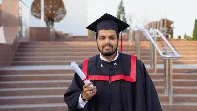 A young indian male graduate with diploma against the background of university