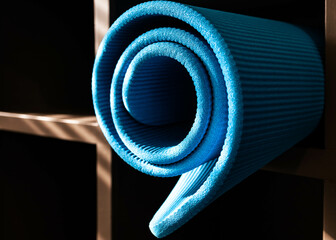 Closeup a blue yoga mat rolled on the shelf after class with natural sunlight shining through the window. Indoor exercise at the gym. Healthy lifestyle concept. Fitness equipment storage.