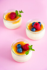 French custard dessert creme brulee with crispy caramel crust and fresh berries on a pink background.