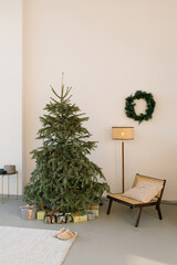 Fototapeta na wymiar Christmas tree, a cozy armchair, a lamp and a wreath on the wall in a modern living room