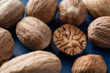 Whole and halved nutmeg seeds over blue background. Macro. Muscat nuts closeup. Spice and seasoning concept. Dry fruits of myristica fragrans tree for cooking and herbal medicine. - obrazy, fototapety, plakaty