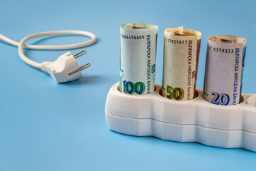 Bulgarian lev banknotes plugged into a white power strip over blue background. Increasing cost of electricity in Bulgaria. Rise in electricity prices, energy costs concept.