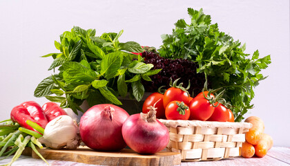 Fresh seasonal greens and cherry tomatoes in a wicker basket in front of a black background, mint, parsley, pepper, carrot, lettuce