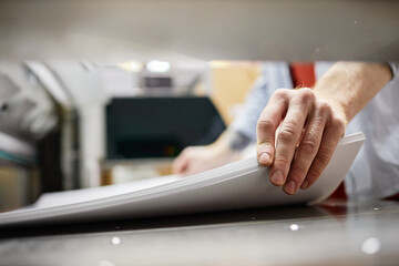 Close up of man putting stack of paper in printing machine at publishing shop, copy space