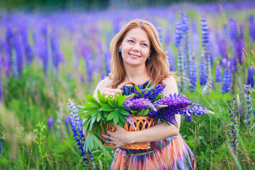 Young attractive woman holding a basket full of lupine flowers in her hands