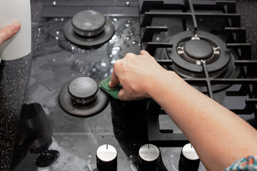 A housewife cleans the kitchen gas stove with a sponge. Maintenance of tempered glass and glass ceramics