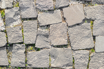 Texture of masonry roads made of asymmetrical stones with grass between masonry. Top view